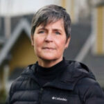 A portrait photo of a woman with gray hair, wearing a puffy jacket who is happy with the work Applied Roofing Science did