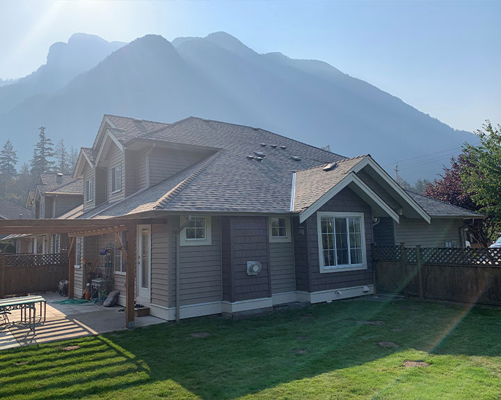 A modern new build house with sloped roofing against the backdrop of BC mountains